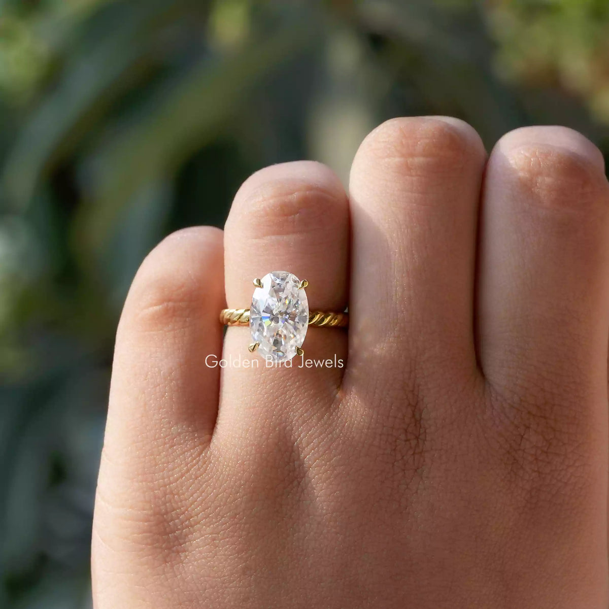 Oval-cut moissanite solitaire ring on hand, gold-tone band with oval stone in 4-prong setting