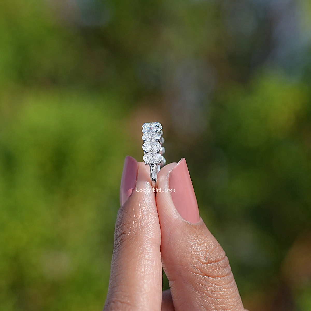 14K white gold half eternity ring with oval moissanite stones, on fingertip