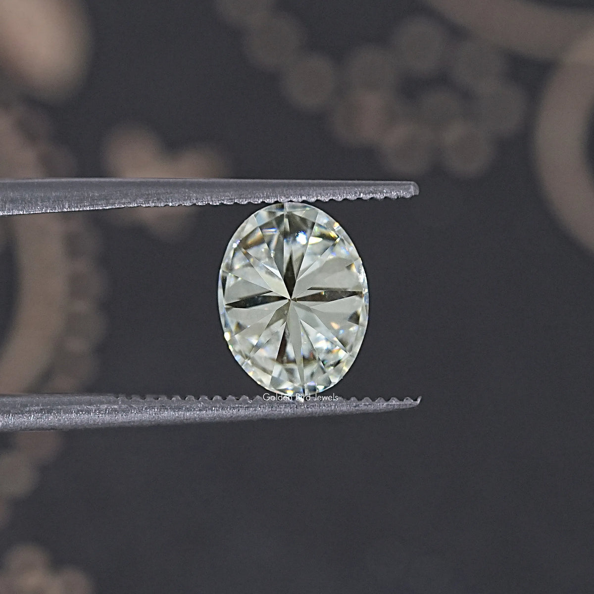Oval moissanite loose stone, clear white facets held by metal tweezers
