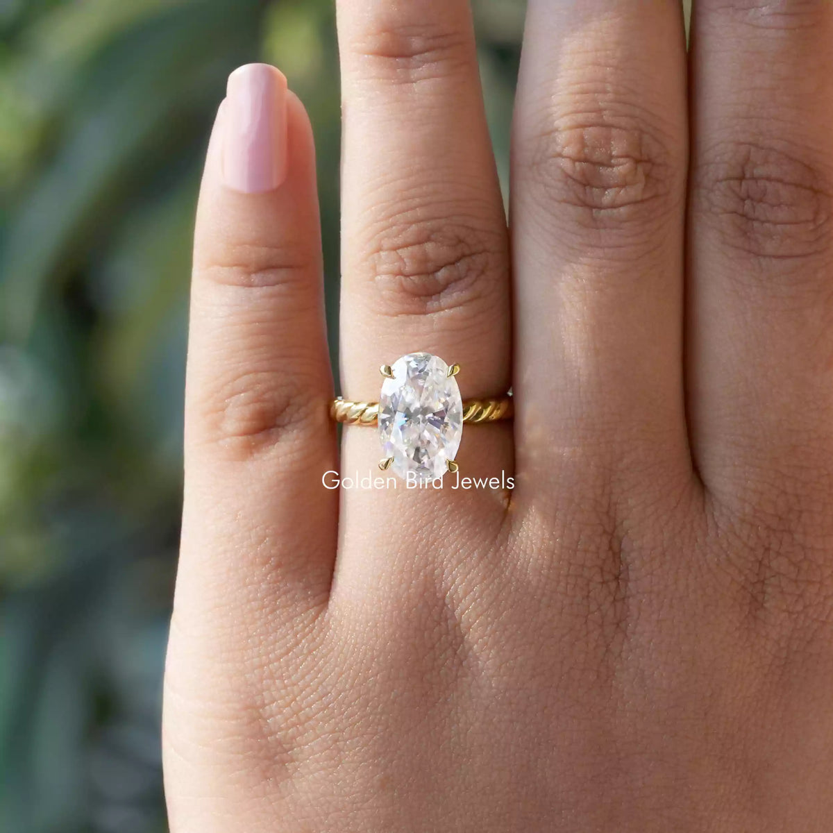 Oval-cut moissanite solitaire ring on finger, gold-tone band with 4-prong setting