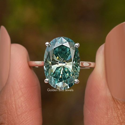 Sterling silver oval moissanite solitaire ring with teal center and four prongs.