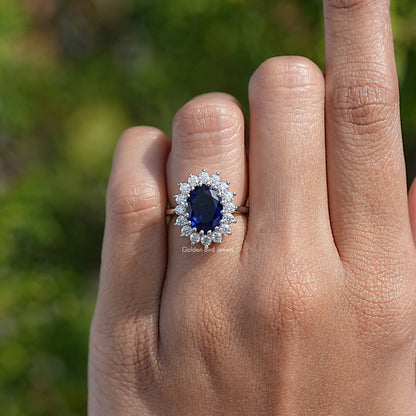 Oval blue center halo engagement ring with silver band, shown from front on fingers