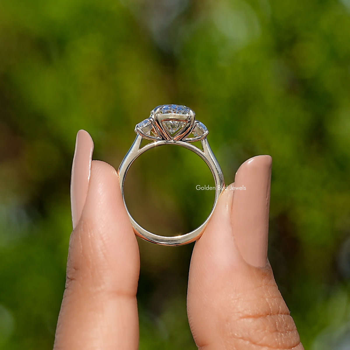 Three-stone diamond engagement ring from behind, prong-set center and side stones