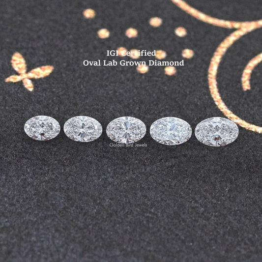 Five oval-cut loose lab diamonds arranged in a row on dark fabric