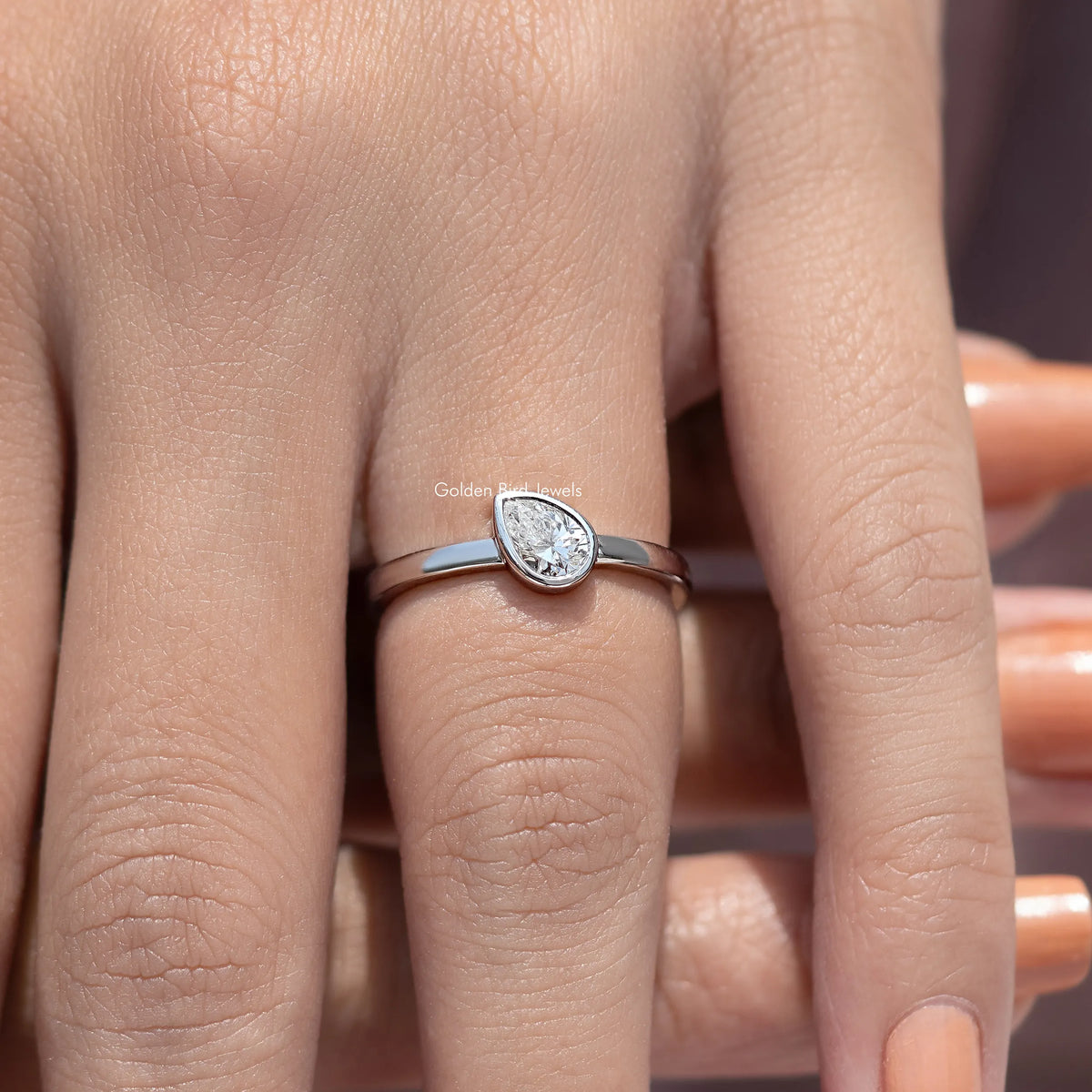 Silver solitaire ring with bezel-set pear-shaped diamond, slim band view from front