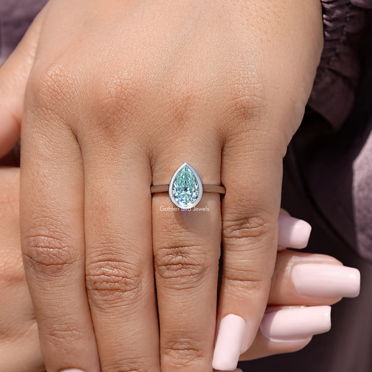 Sterling silver bezel-set solitaire ring with pear-cut light blue stone on hand