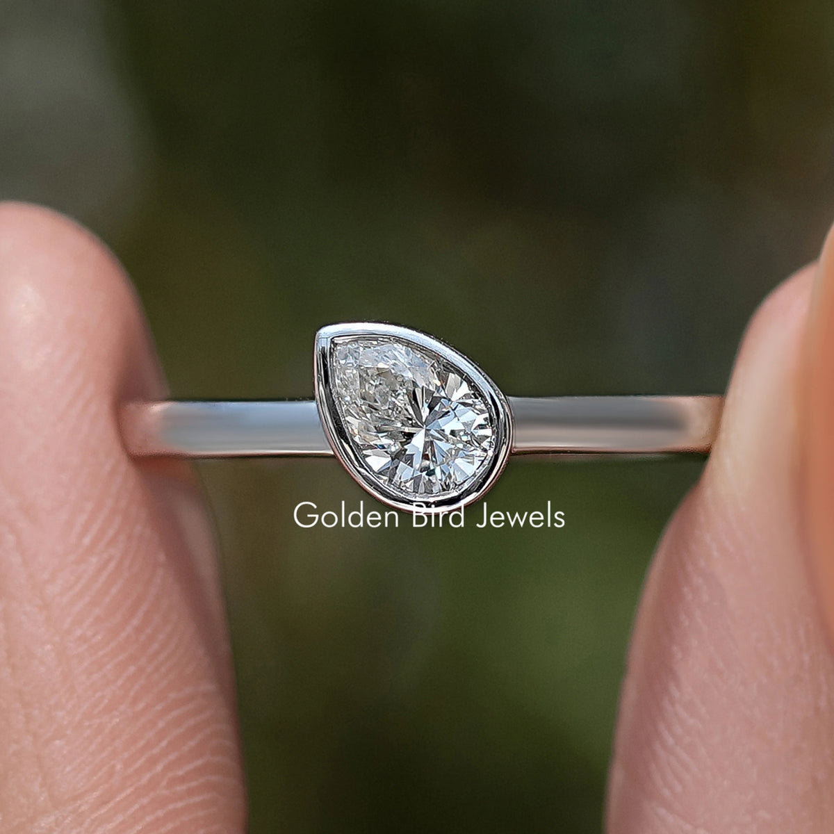 Close-up silver solitaire ring with bezel-set pear-shaped diamond and slim band