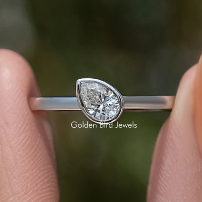 Close-up silver solitaire ring with bezel-set pear-shaped diamond and slim band