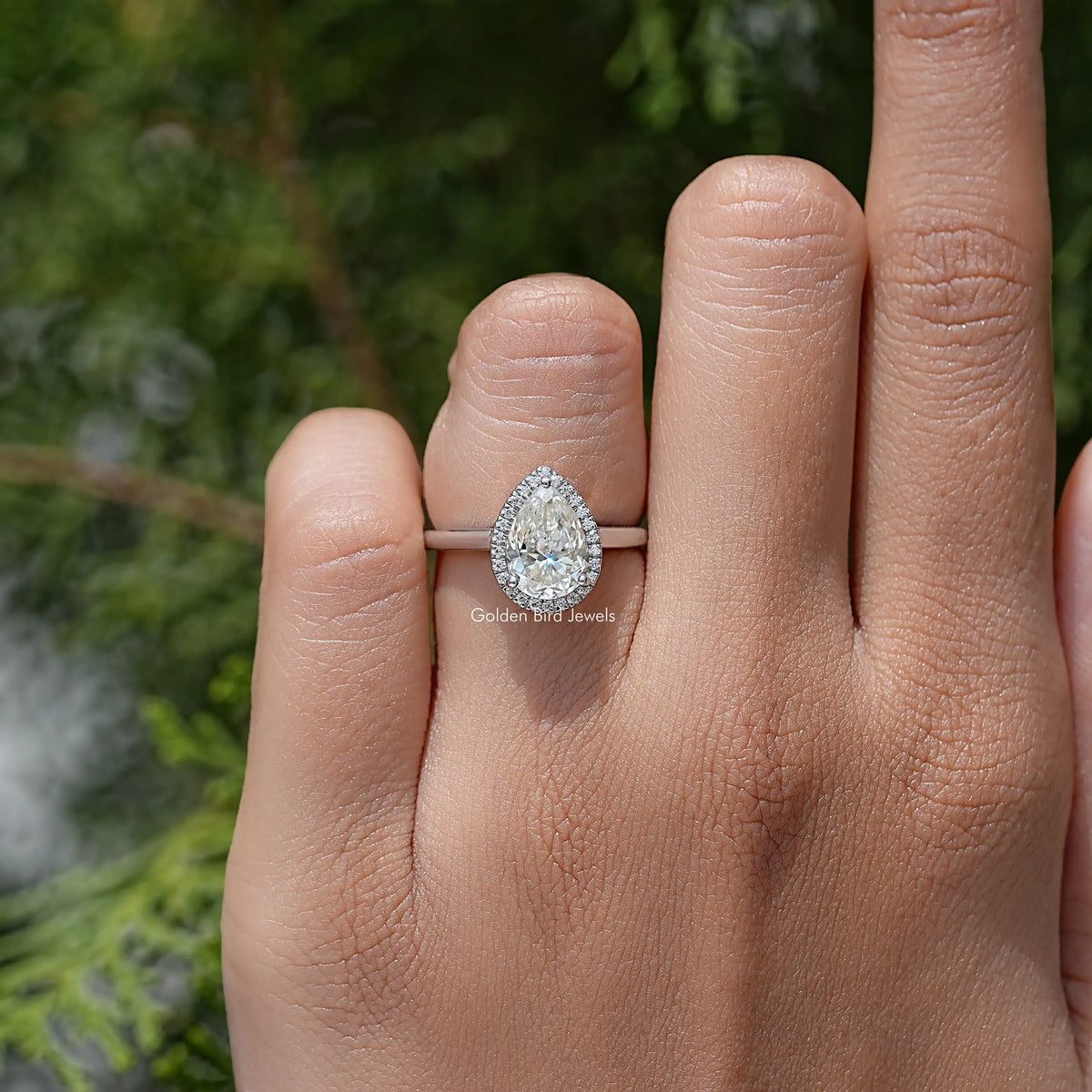 Pear-cut moissanite halo engagement ring on hand, pear center stone in prongs
