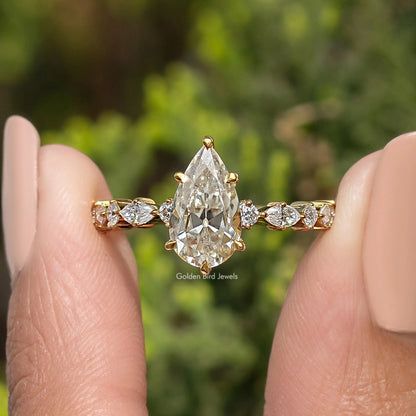 Moissanite engagement ring featuring a pear-cut center stone and small side stones, gold-tone