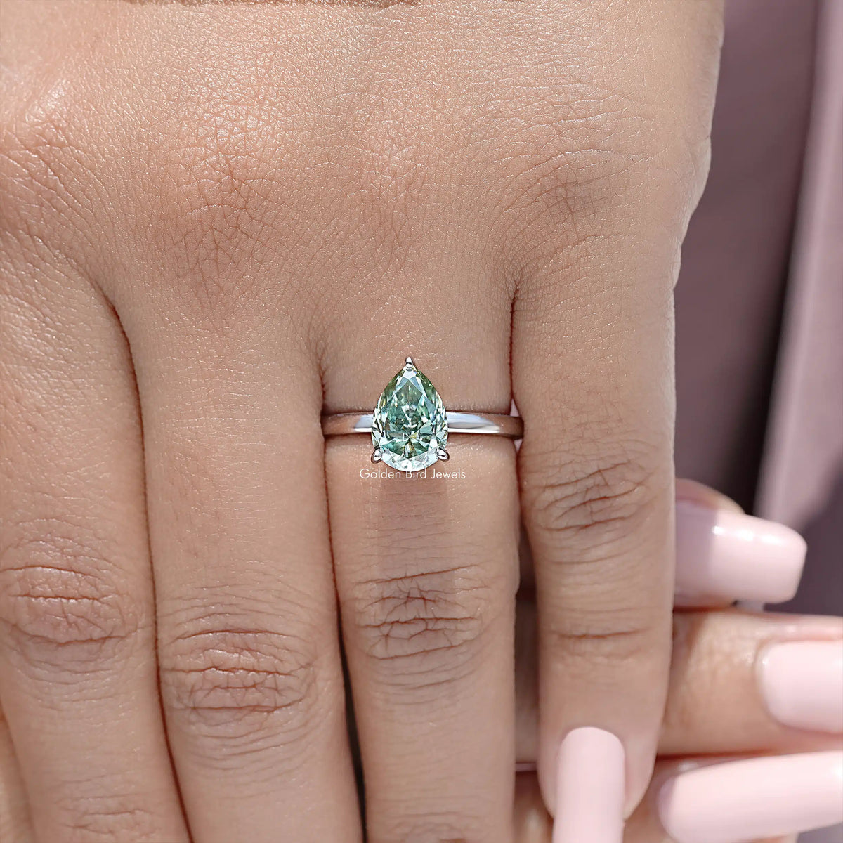 Close-up of sterling silver pear-cut moissanite engagement ring band, green center stone