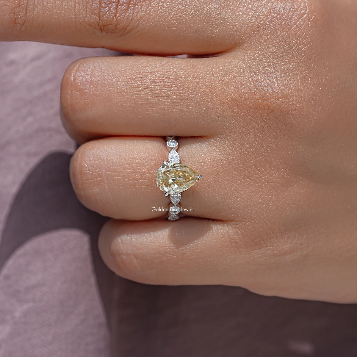 Close-up of yellow pear-cut moissanite engagement ring with small side accents