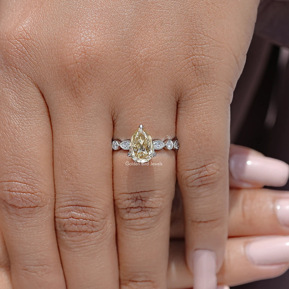 Yellow pear-cut moissanite engagement ring with round side stones on hand