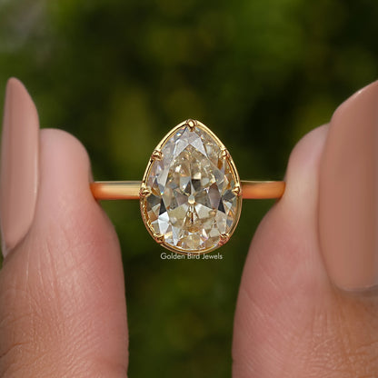 Gold-tone pear moissanite solitaire engagement ring held between fingertips