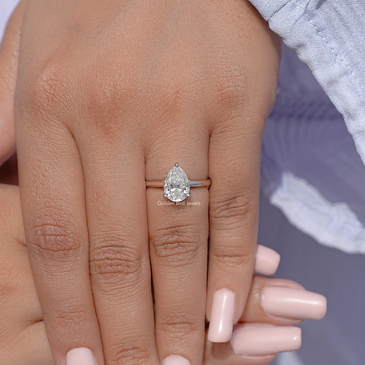Pear-cut solitaire engagement ring on finger, clear pear-shaped stone in silver setting