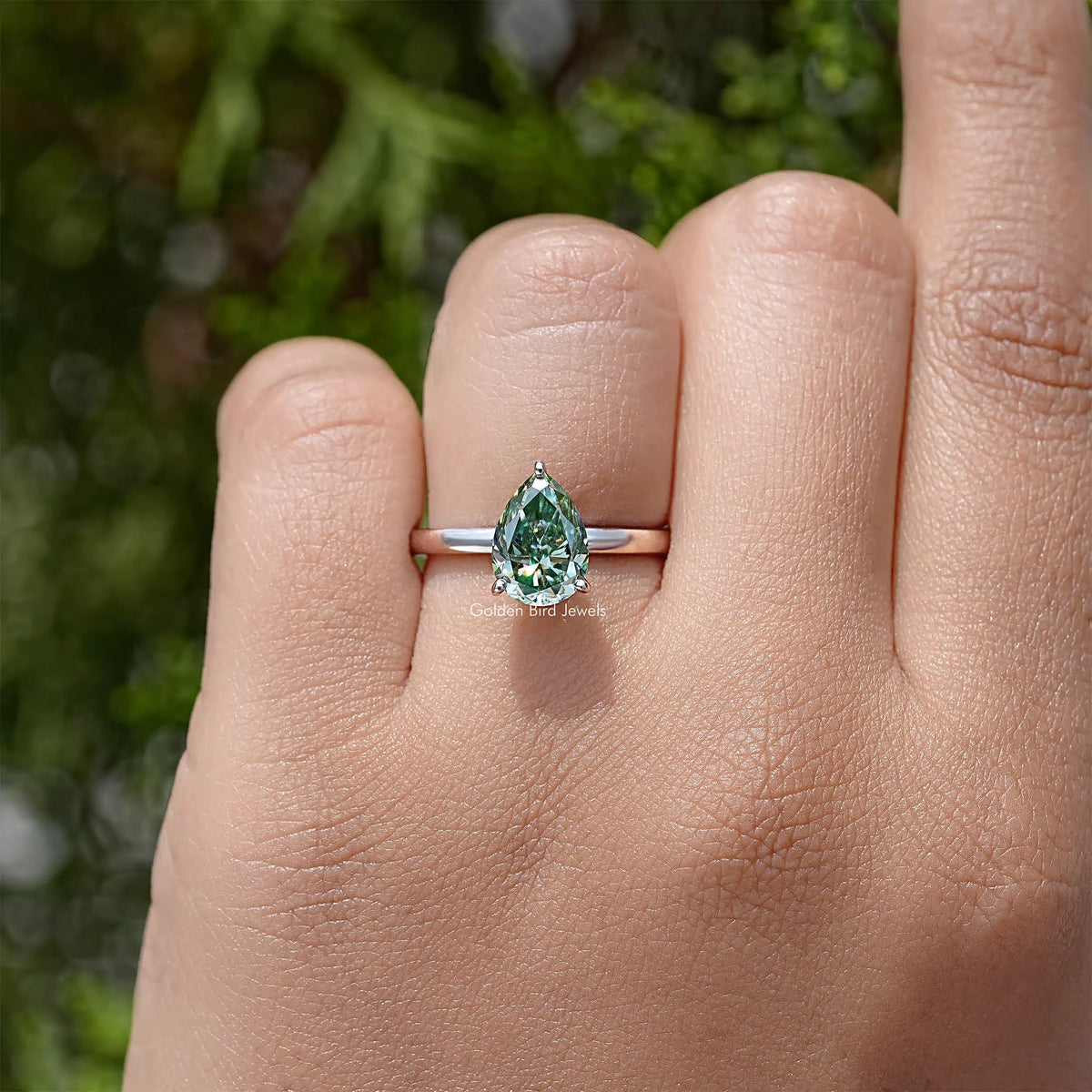 Sterling silver pear-cut moissanite engagement ring on hand, green center stone