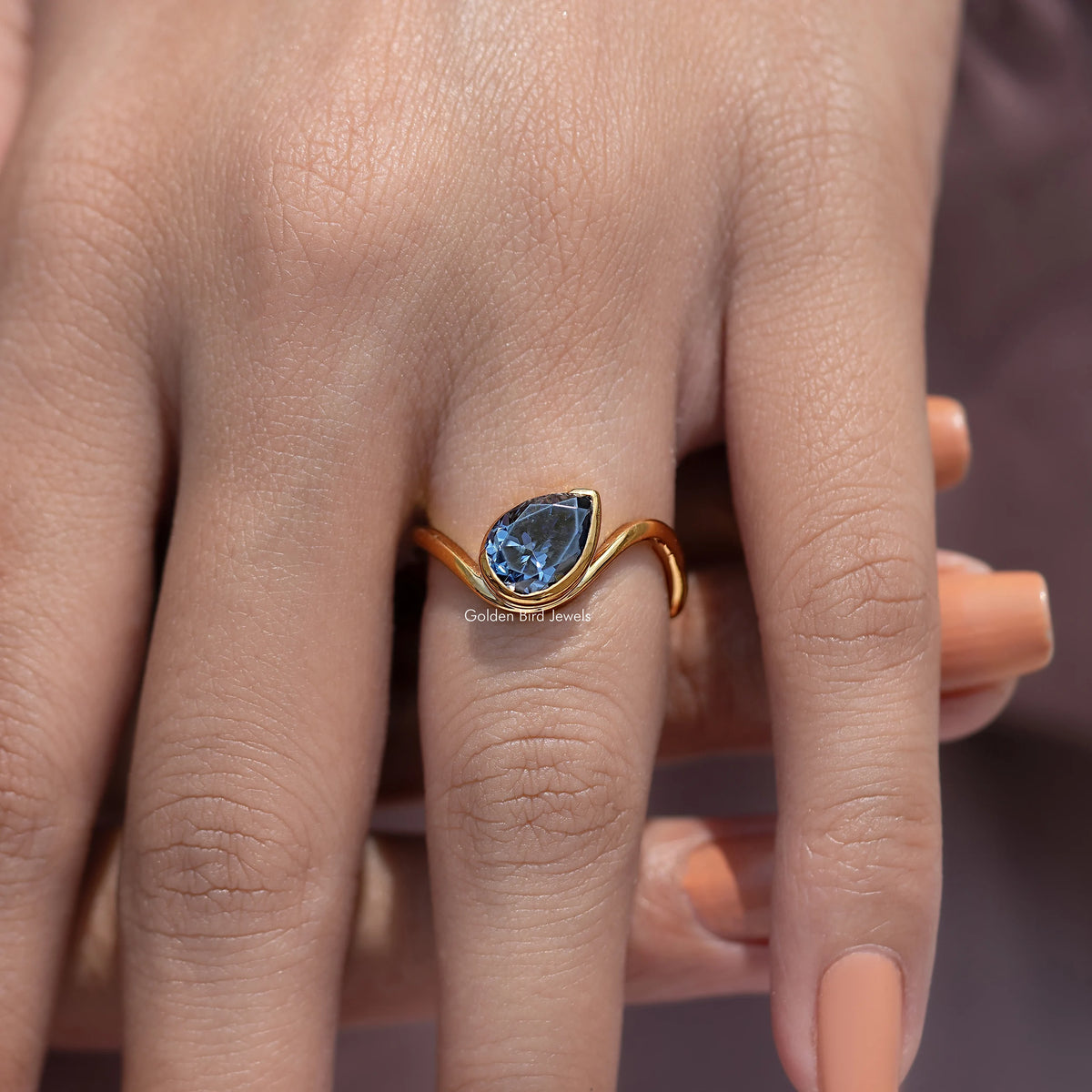 Curved solitaire ring with blue gemstone on fingers, gold open band