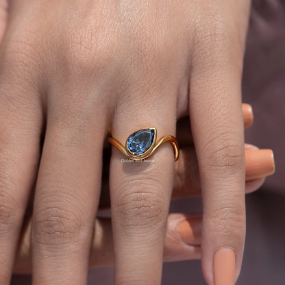 Curved solitaire ring with blue gemstone on fingers, gold open band