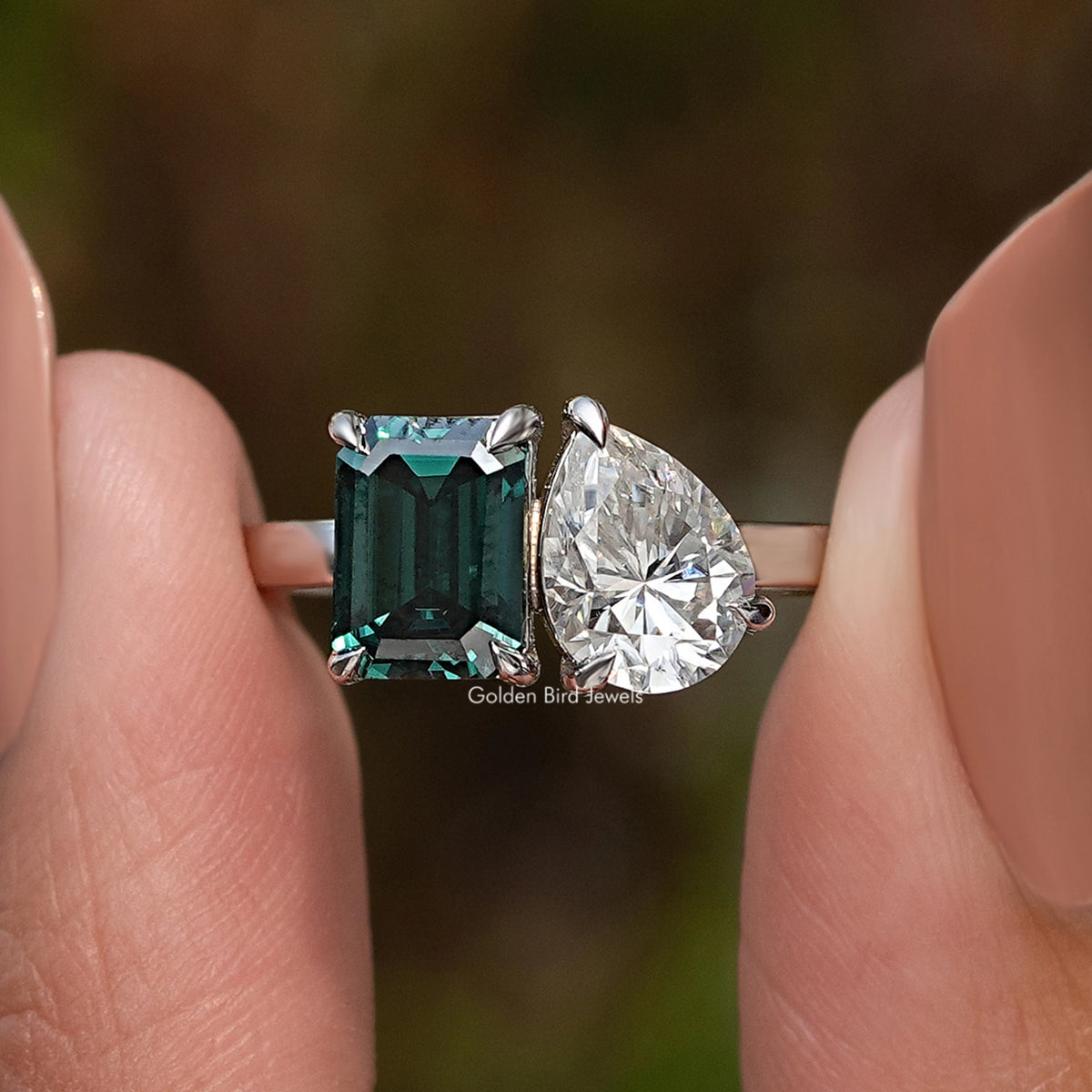 Two-stone ring detail: emerald-cut green stone with large pear-cut clear stone