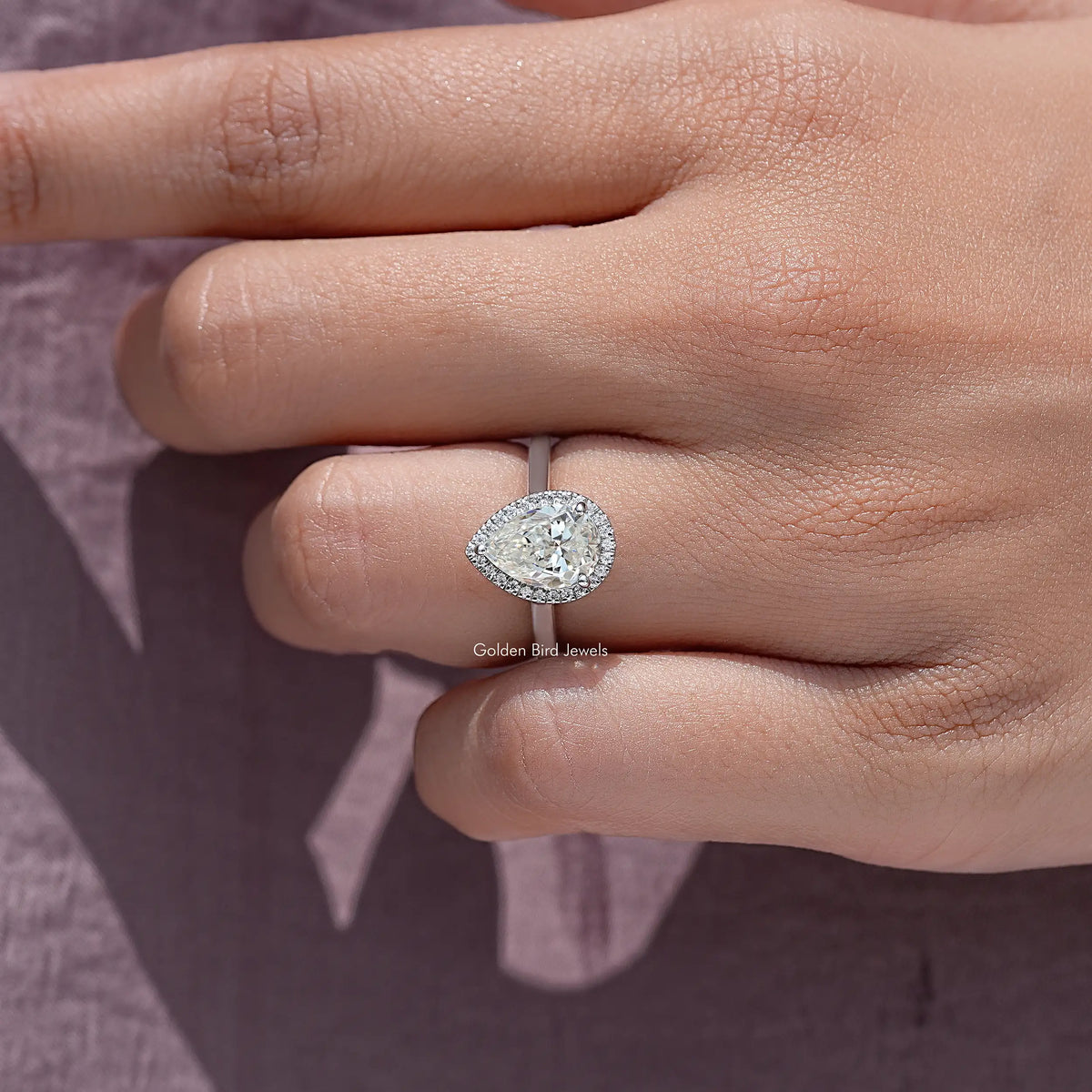Pear-cut moissanite halo ring on fingers, oval halo with pave detail, silver