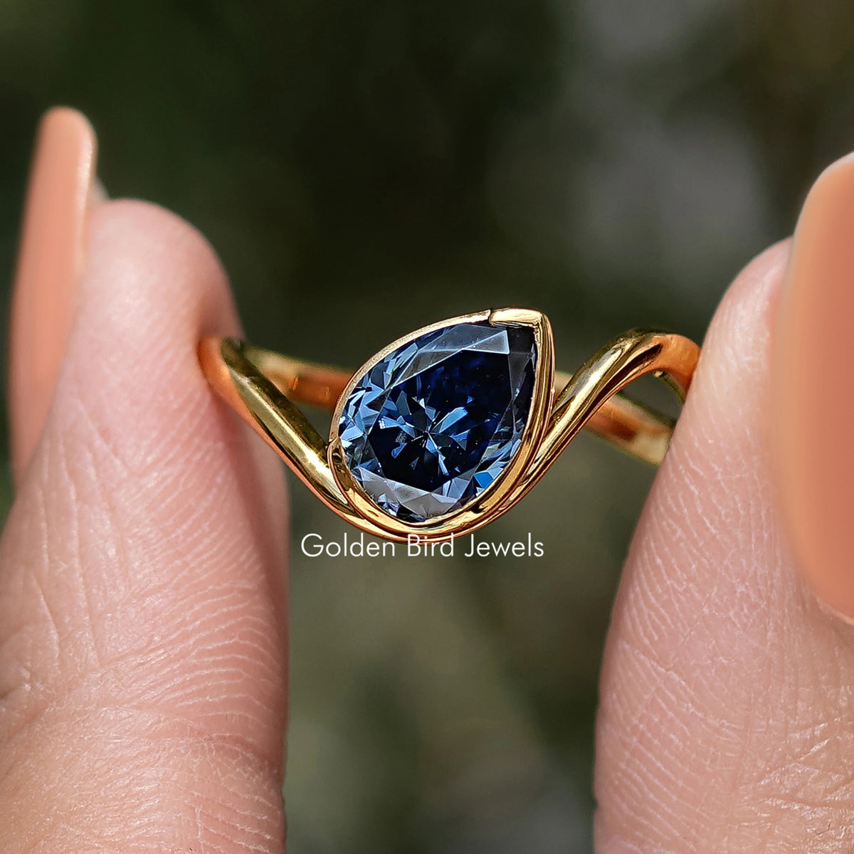 Curved solitaire ring with large blue pear-cut gemstone and gold band