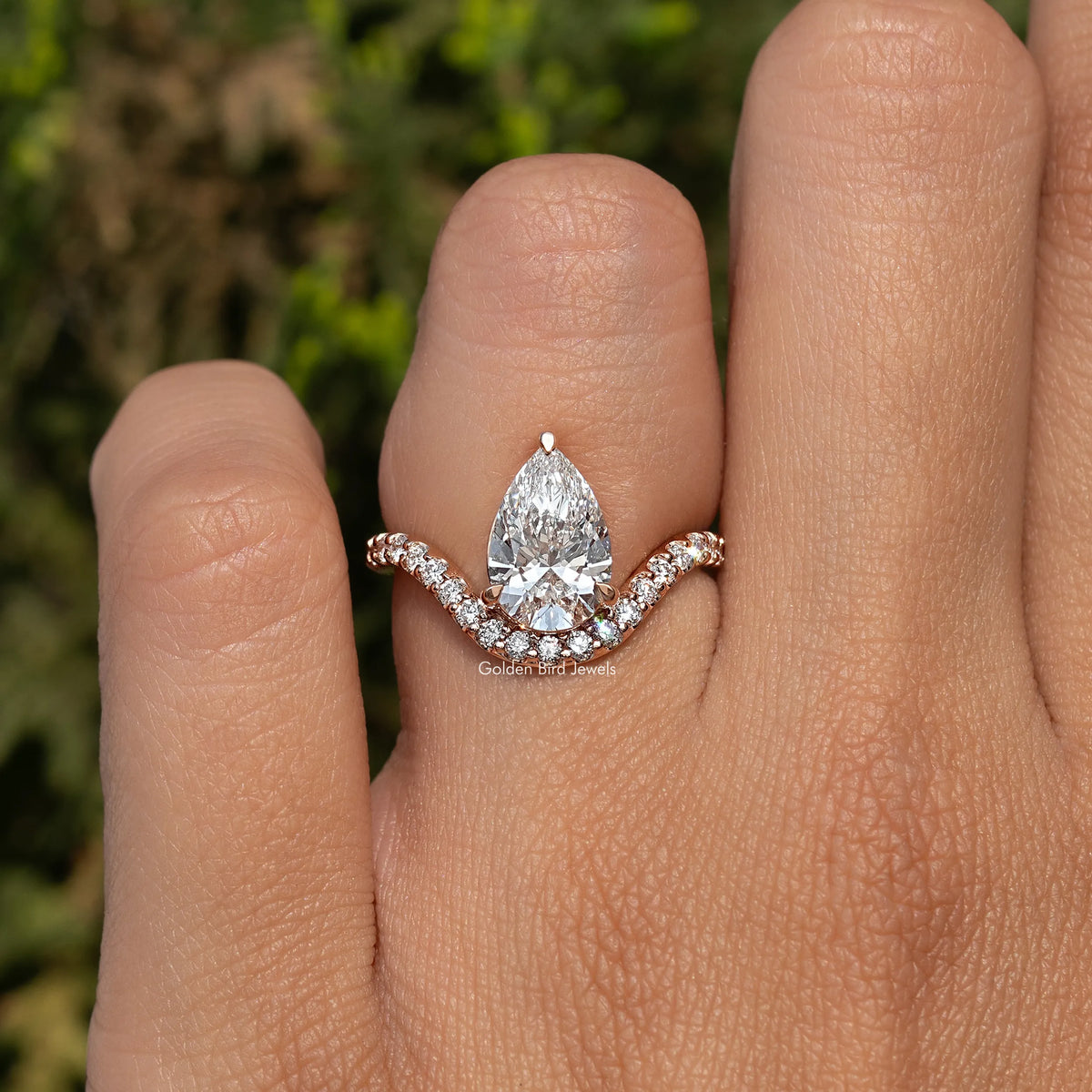 Pear-cut engagement ring on hand, rose-gold tone band with curved halo accents