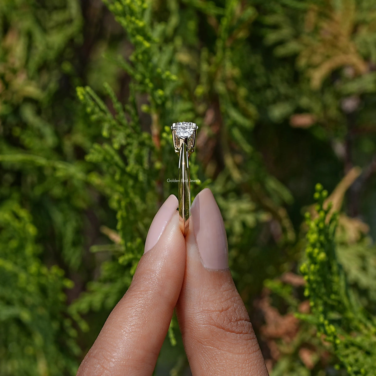 Side View of Pear Cut Lab Diamond Three Stone Engagement Ring In two fingers