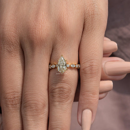 Pear-cut moissanite engagement ring with round side stones on a slim gold-tone band