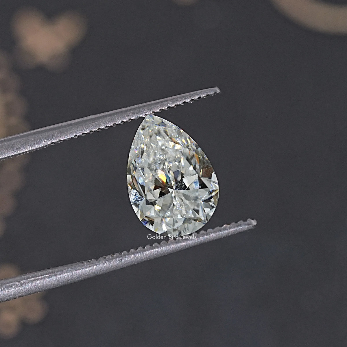 Near colorless pear-cut moissanite loose gemstone held by tweezers