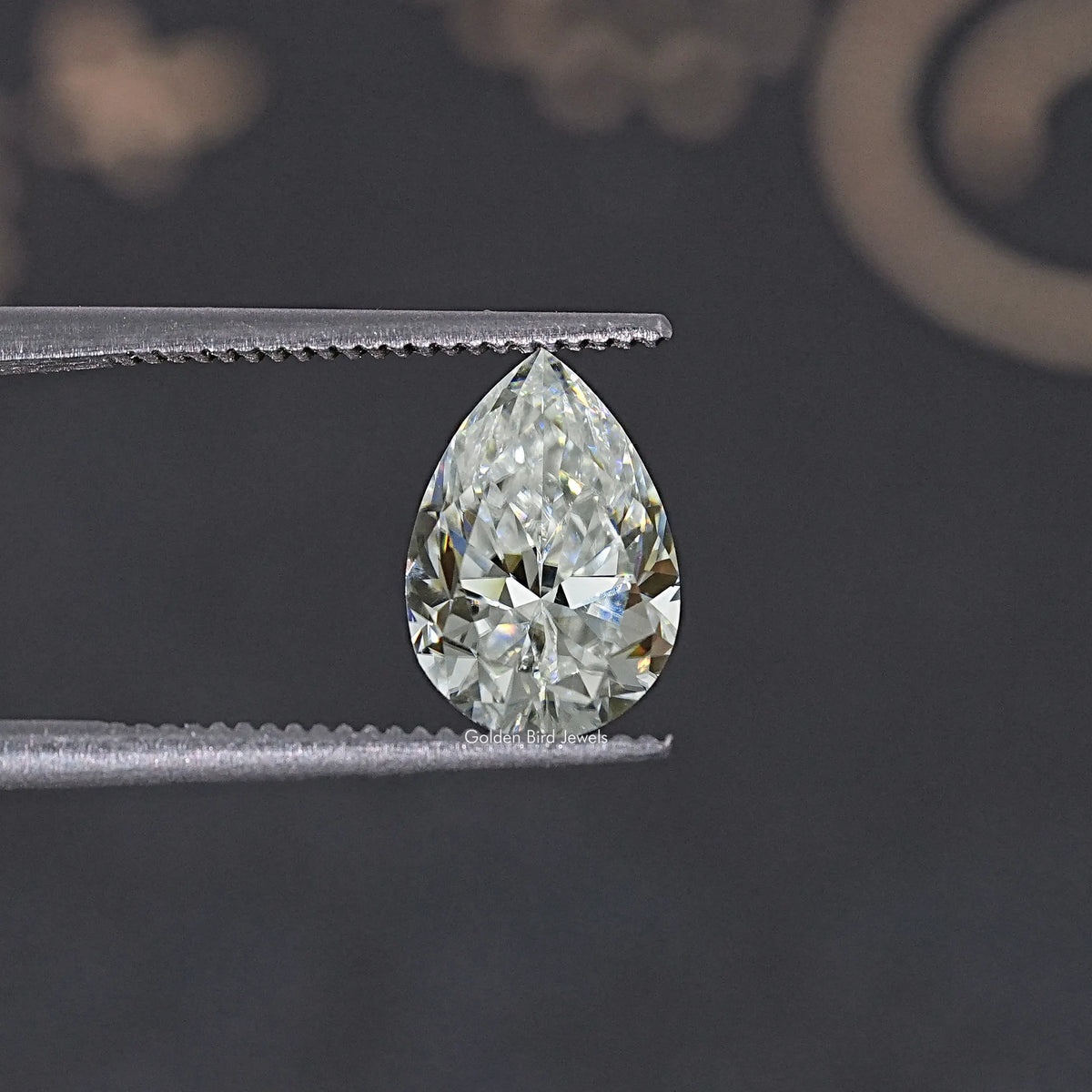 Pear-cut colorless moissanite held between metal tweezers.