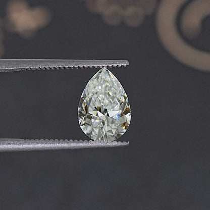 Pear-cut colorless moissanite held between metal tweezers.
