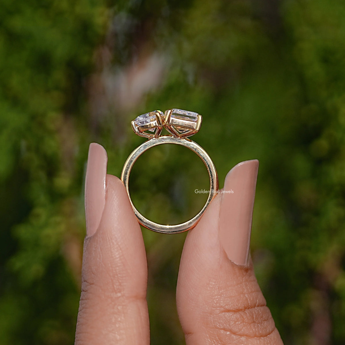 Gold-tone two-stone ring with emerald-cut moissanite and pear-cut accent, on fingers