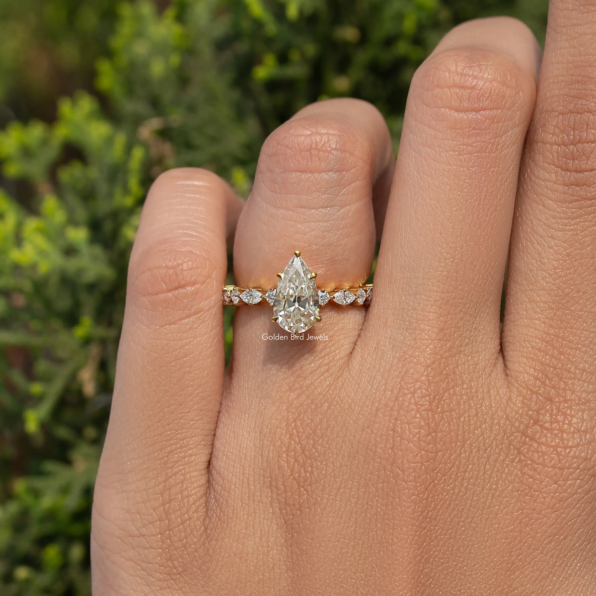 Moissanite engagement ring with pear-cut center and round side stones, gold-tone band
