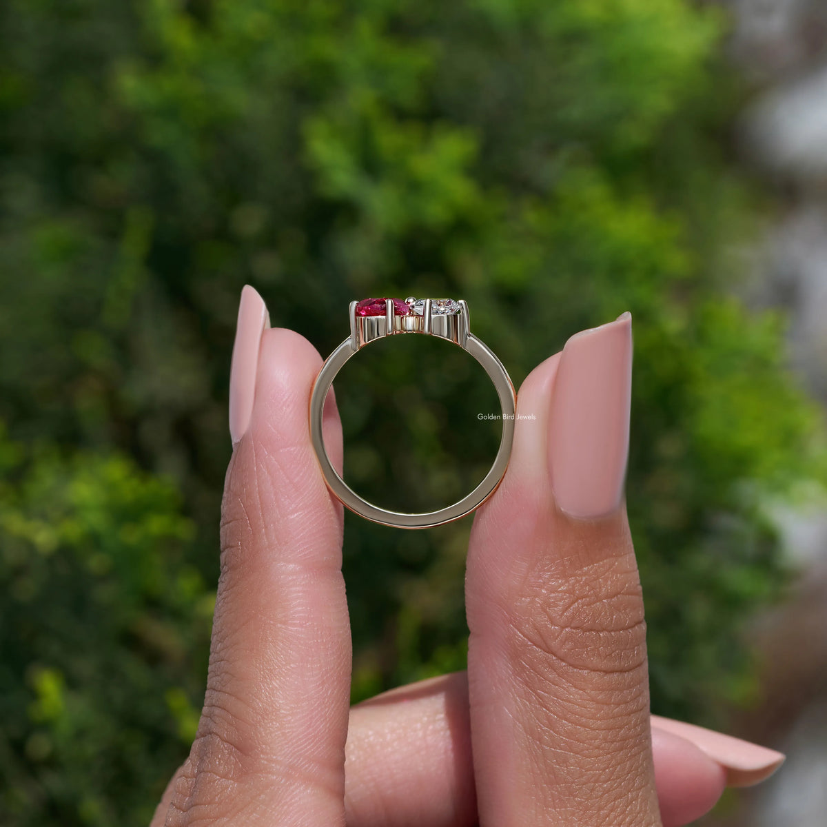 Gold-tone engagement ring featuring a red pear-cut center stone and diamond side sparkle