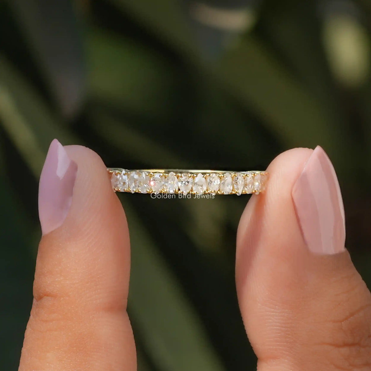 Half-eternity moissanite band held between fingers, prong-set stone row