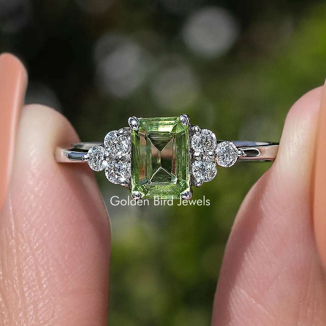 Green emerald-cut gemstone ring with round halo and prong setting, silver band