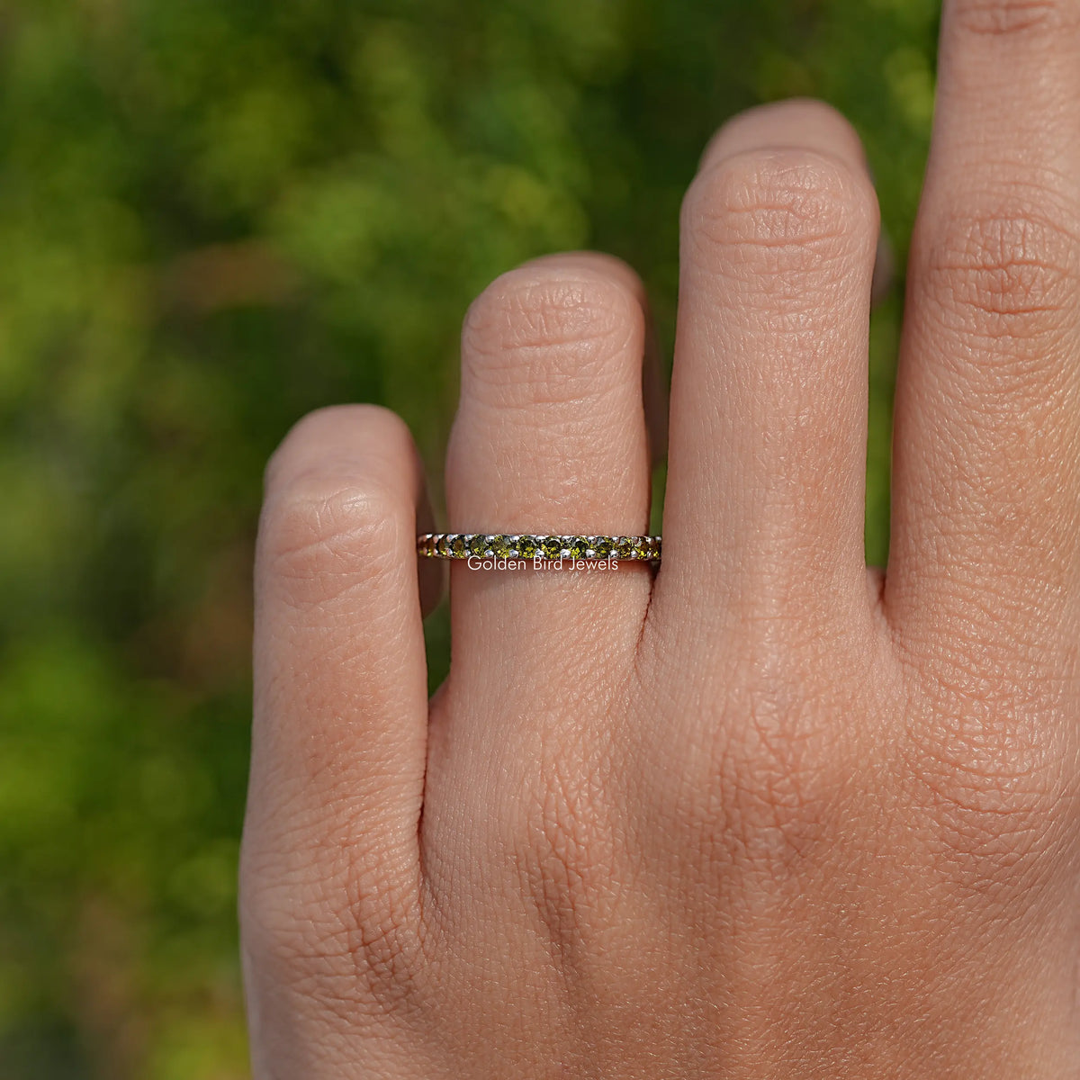 Green-stone eternity band ring with round stones across the top