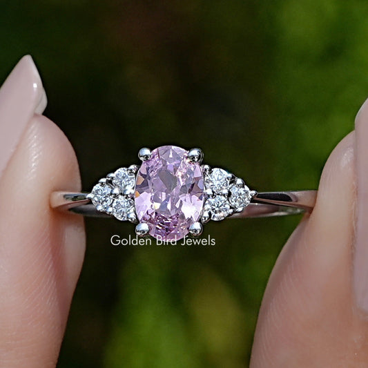 Close-up of prong-set oval pink center gemstone with round side stones on silver band