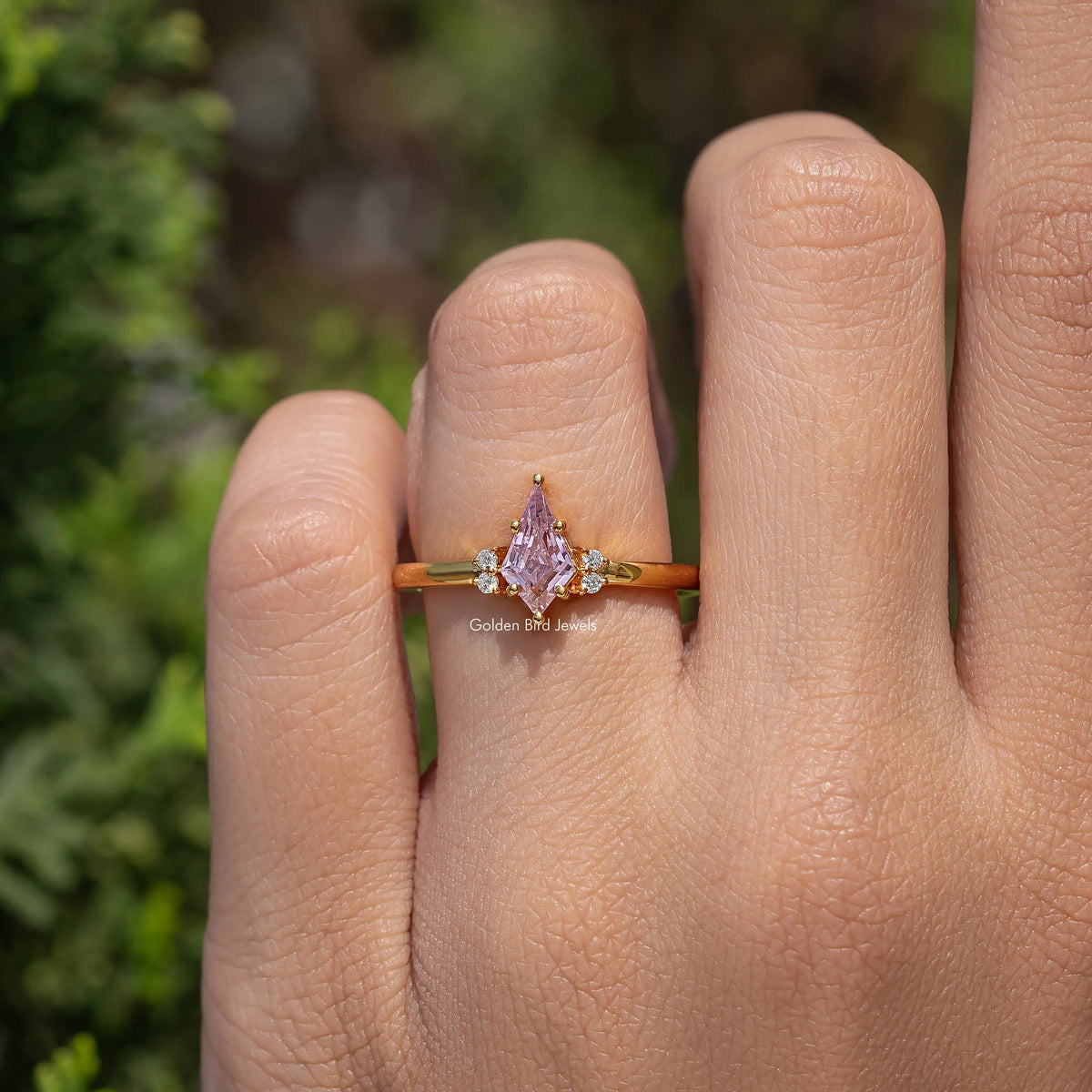 Gold ring with pink kite-cut center stone and three-stone style sparkle