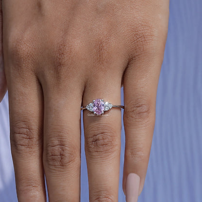 Oval pink gemstone engagement ring on hand with round side stones and slim band
