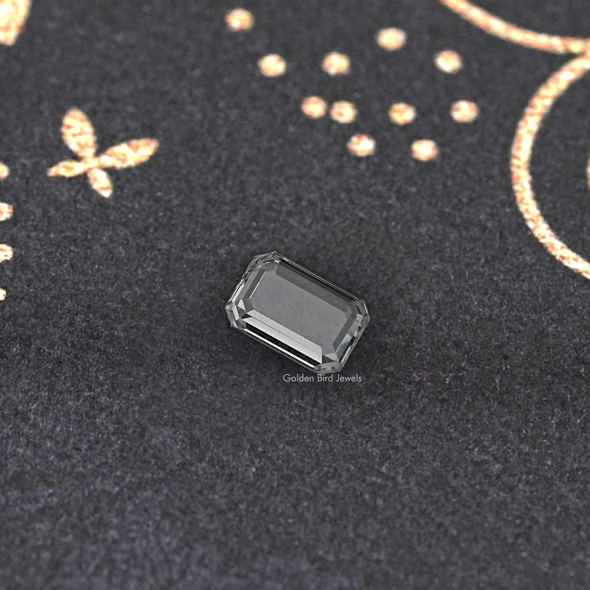 Emerald-cut loose diamond close-up, clear rectangular facets on dark fabric