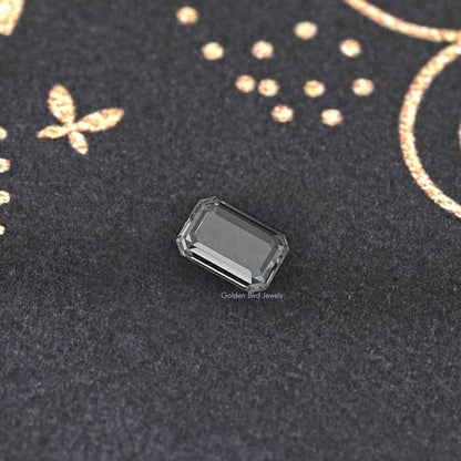 Emerald-cut loose diamond close-up, clear rectangular facets on dark fabric