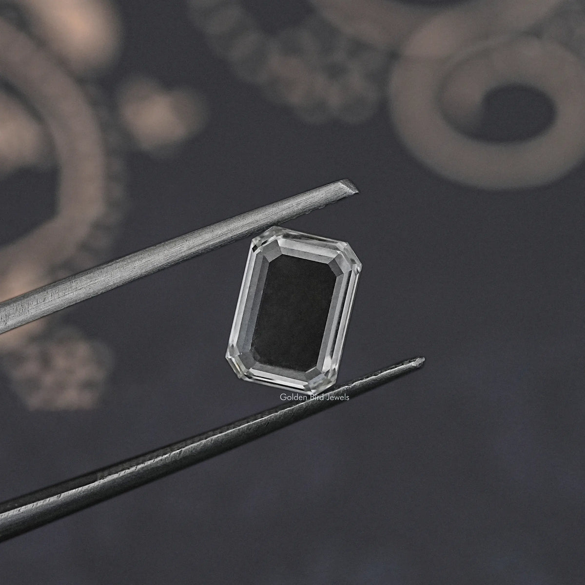 Emerald-cut loose diamond between metal tweezers, clear side profile close-up