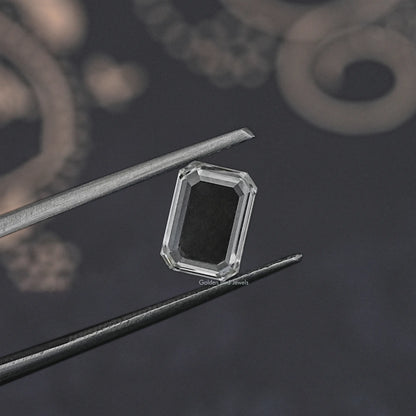 Emerald-cut loose diamond between metal tweezers, clear side profile close-up