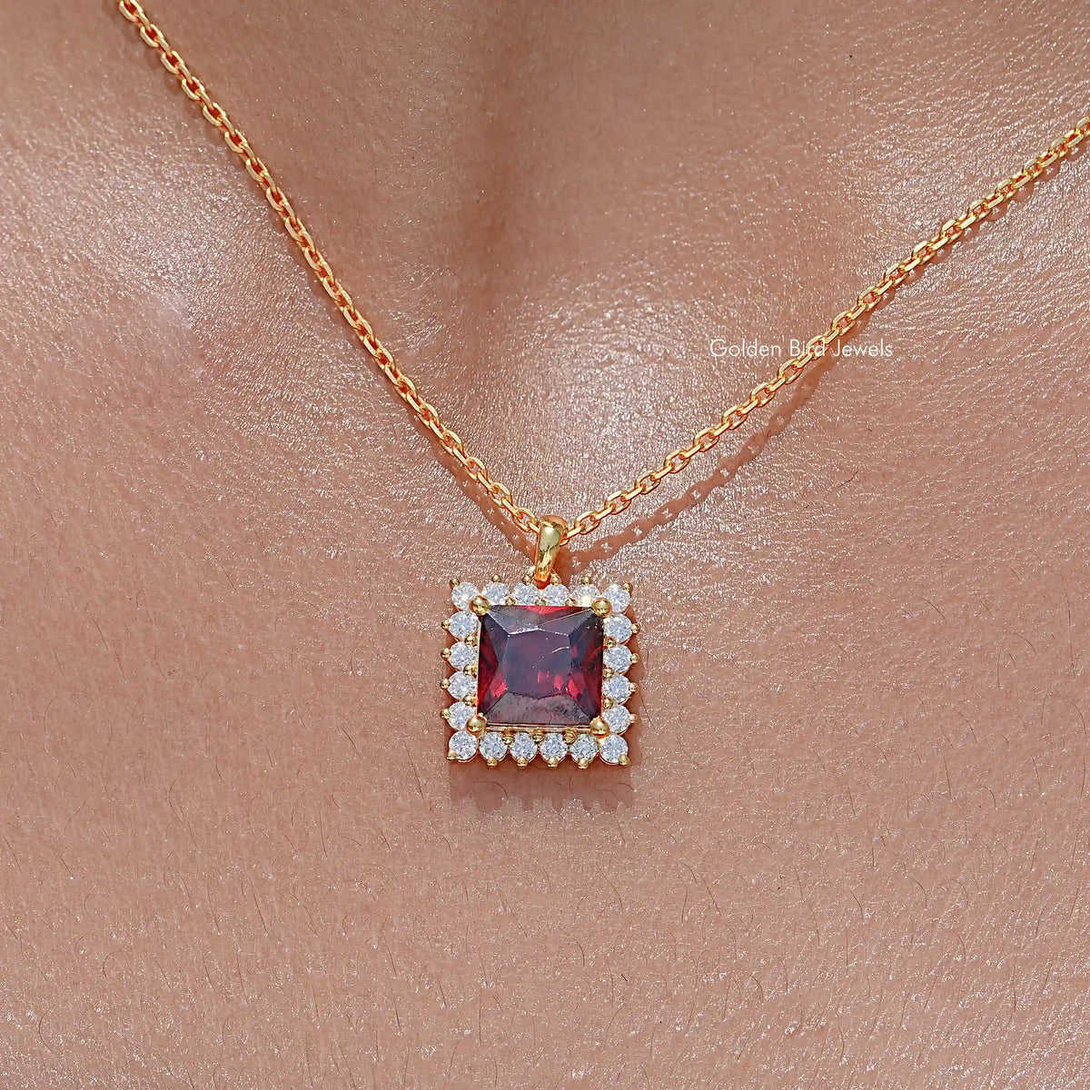 Square ruby-red gemstone pendant with clear stone halo on gold chain