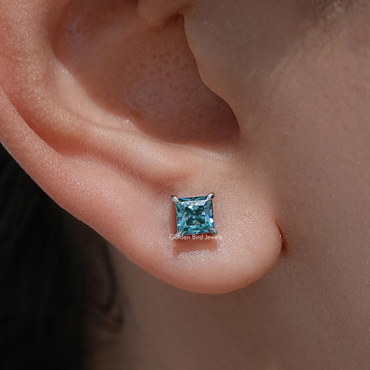 Screw-back stud earrings with blue princess-cut gemstone on visible earlobe