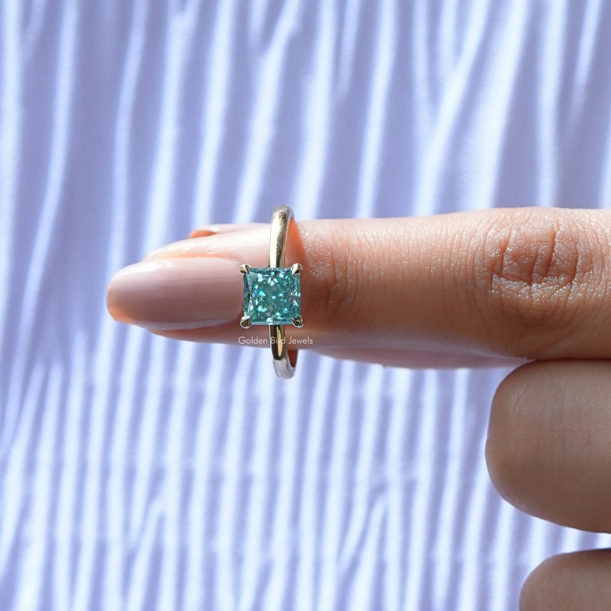 Silver princess-cut solitaire ring on finger, cyan-blue square moissanite centerpiece