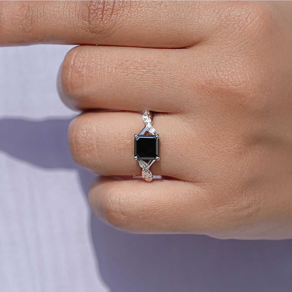 Close-up of black asscher-cut center stone with prong-set side stones on silver band