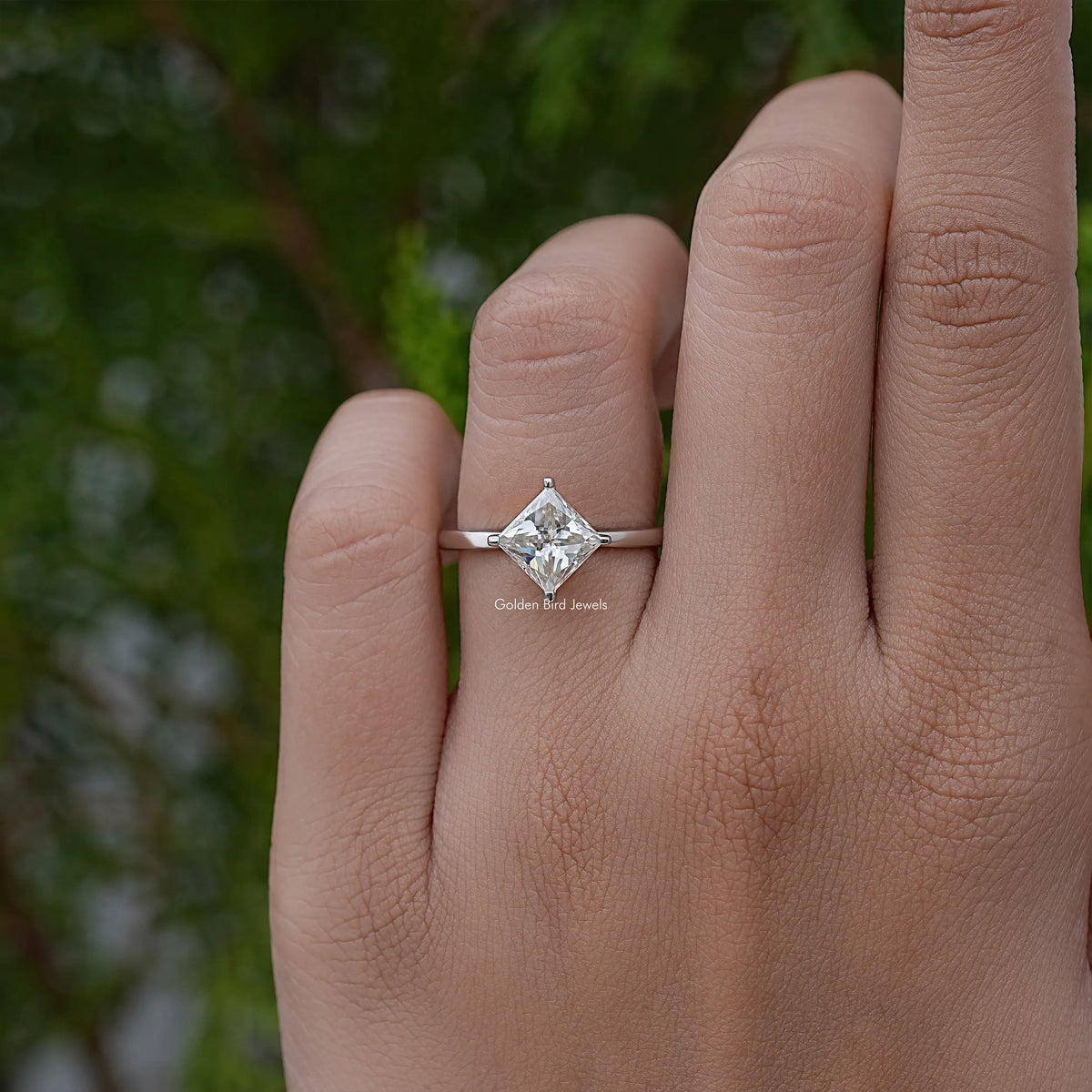 Princess-cut solitaire engagement ring with square center stone on finger, silver band