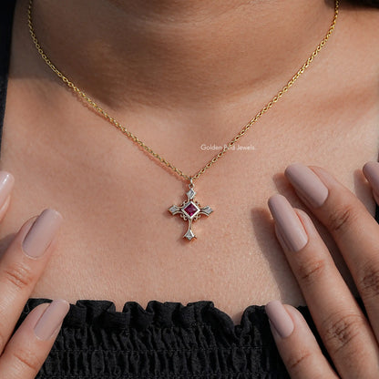 Square red gemstone cross pendant on gold chain over black ruffled neckline